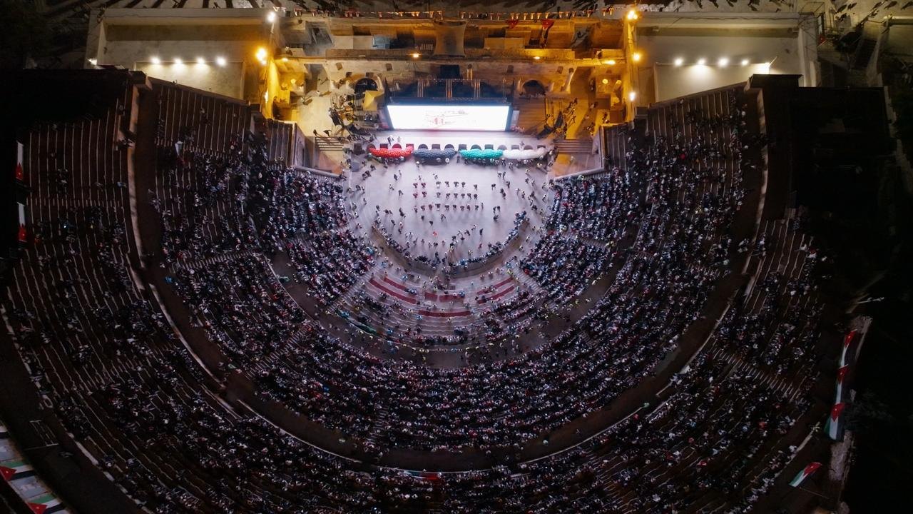Aerial view of the Roman Theatre in Amman, its tiered stone seating filled to capacity at night.